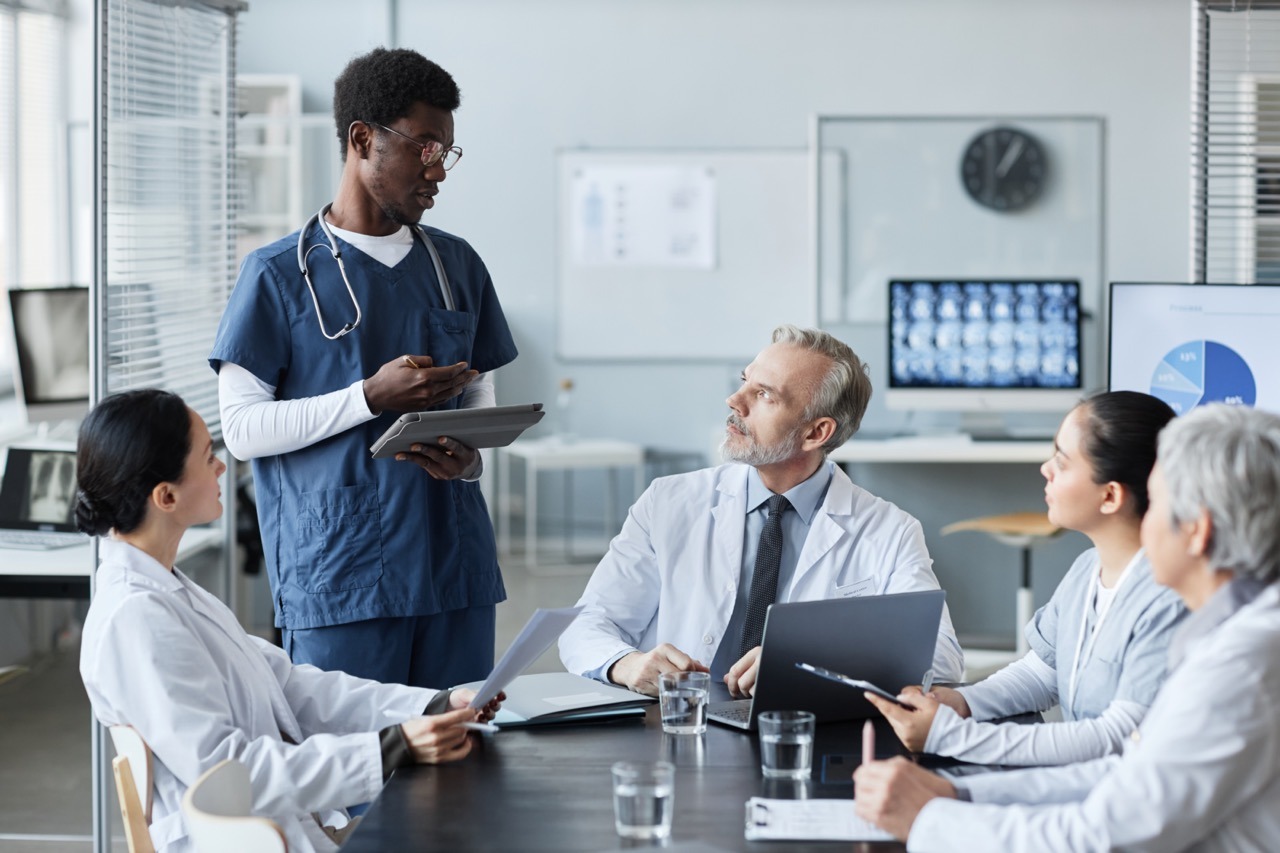 Young confident African American male intern with tablet making speech A HIPAA contingency plan document open beside a hospital downtime workstation