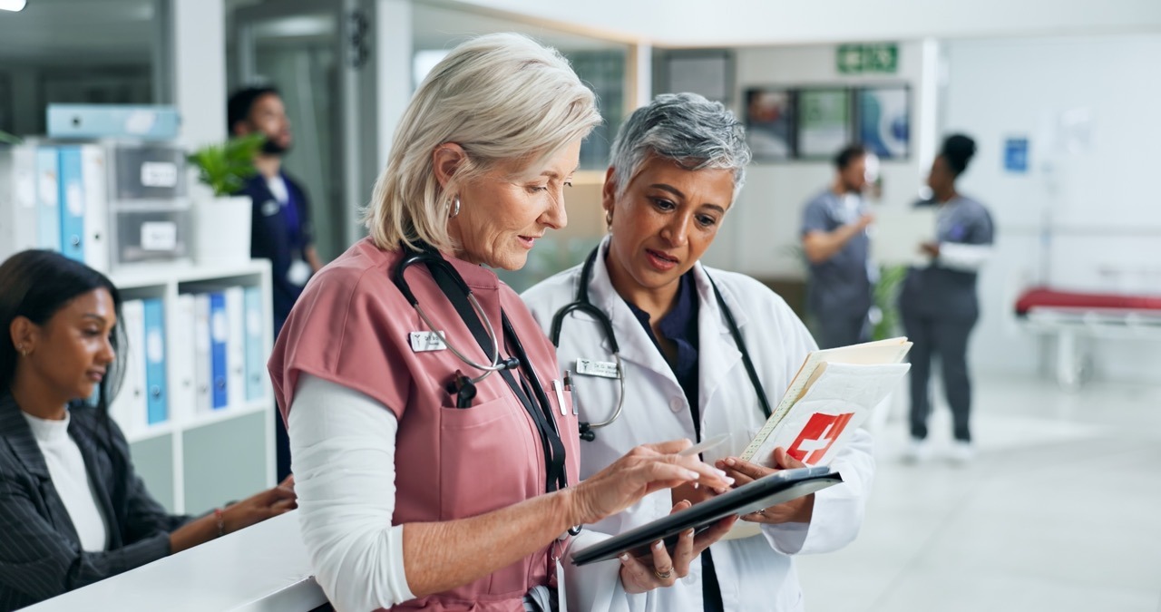 Nurse and physician reviewing digital patient intake on a tablet at a hospital registration desk